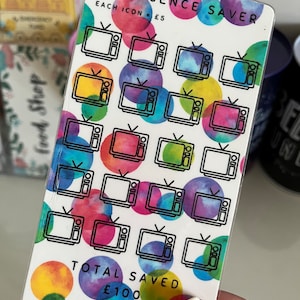 May include: A white card with a colorful watercolor background and black outlines of televisions. The card says "TV Licence Saver" and "Each Icon = &pound;5". There are 20 televisions on the card. The card also says "Total Saved &pound;100" and "Budgets by Steph".