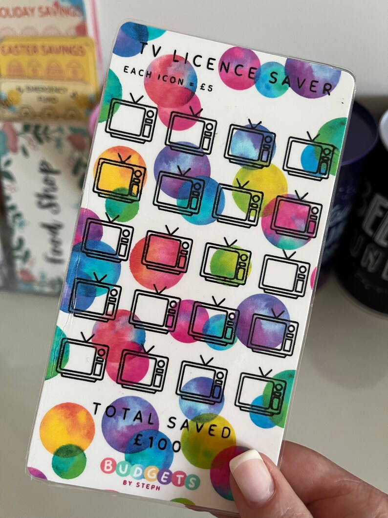 May include: A white card with a colorful watercolor background and black outlines of televisions. The card says "TV Licence Saver" and "Each Icon = &pound;5". There are 20 televisions on the card. The card also says "Total Saved &pound;100" and "Budgets by Steph".