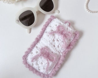 Puede incluir: Estuche para gafas de crochet blanco con ribete de crochet rosa y lazos rosas.