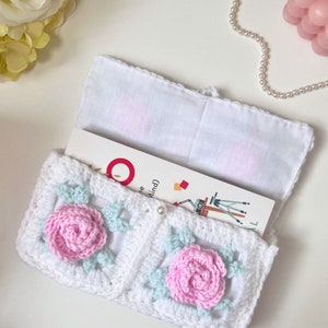 May include: White crocheted book cover with a light blue and pink floral design. The cover is open to reveal a white fabric lining and a book with the text "The Mind".