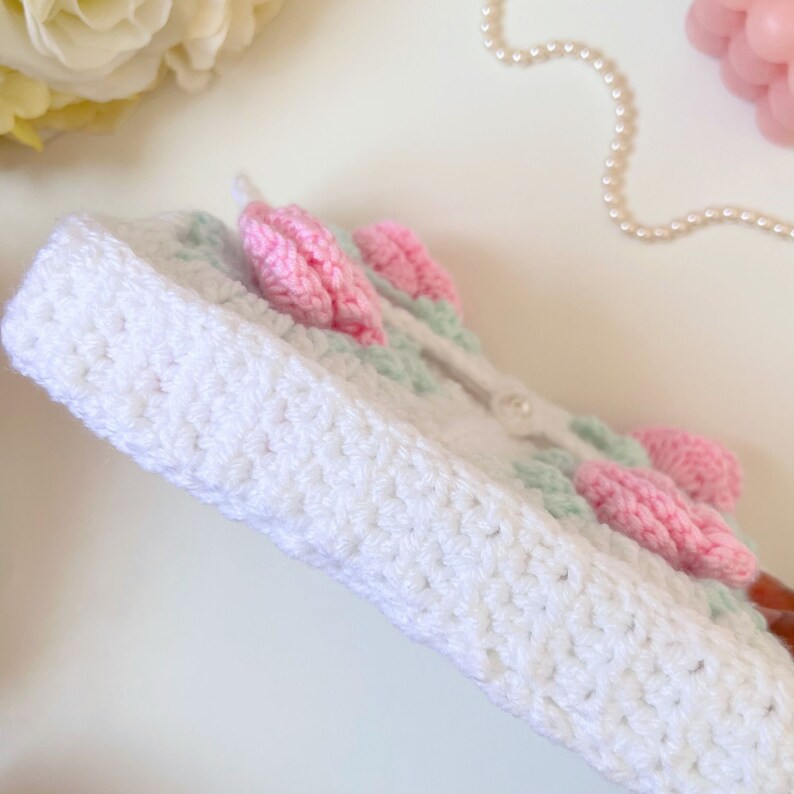 May include: White crocheted box with pink and green flowers. The box has a white button closure.