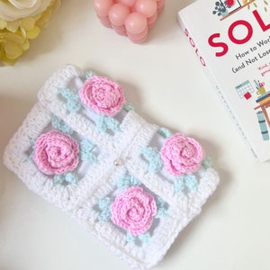 May include: White crocheted pouch with pink and light blue flowers. The pouch has a pearl-like button.