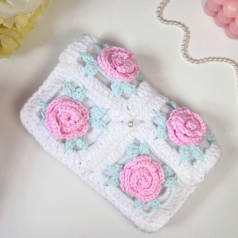 May include: White crocheted clutch with pink and light blue flowers. The clutch has a pearl embellishment.