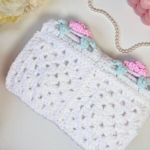 May include: White crocheted bag with a delicate pattern. The bag has a light blue and pink trim with small flower accents.