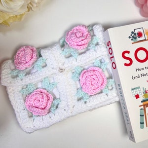 May include: White crocheted square with pink and light blue flowers. The crocheted square is on top of a book titled "SOLO How to Work Alone (and Not Lose Your Mind)" by Rebecca Seal.
