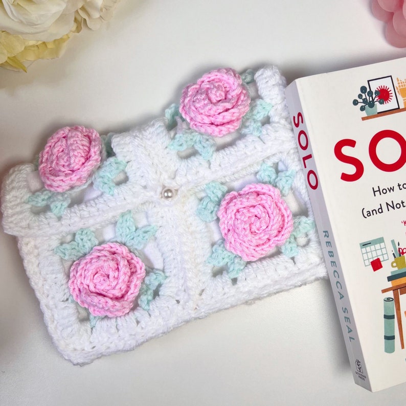 May include: White crocheted square with pink and light blue flowers. The crocheted square is on top of a book titled "SOLO How to Work Alone (and Not Lose Your Mind)" by Rebecca Seal.
