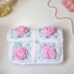 May include: White crocheted clutch bag with pink and light blue flower embellishments.