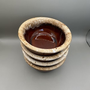May include: A stack of four brown ceramic bowls with a speckled, light-colored rim. The interior of the bowls is a glossy, dark brown. The bowls are stacked on top of each other, with the top bowl angled towards the viewer.