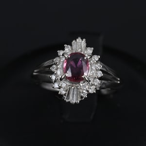 Peut inclure: Une bague en argent ornée d'une pierre précieuse ovale rose foncé au centre, entourée de petits diamants transparents. Le corps de la bague se divise en deux brins délicats de chaque côté.