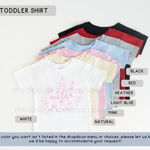 May include: A selection of toddler shirts in colours such as white, black, red, and light blue. The white shirt has a pink graphic with the word "sister". The text "TODDLER SHIRT" is at the top of the image.