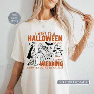 May include: An off-white short-sleeve t-shirt featuring a graphic with the text I WENT TO A HALLOWEEN WEDDING est. 2026, Alexa & Andrew, and And All I Got Was This Boo-tiful Shirt. The design includes illustrations of a couple, bats, and moons.