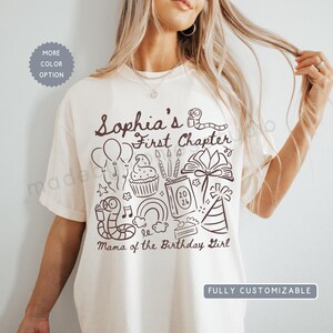 May include: An off-white short-sleeve t-shirt featuring dark brown line art graphics including balloons, a cupcake, a book labeled 2026, a party hat, and worms reading books. The text reads Sophia's First Chapter and Mama of the Birthday Girl.