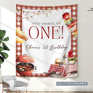 May include: A white banner with a red and white checkered border, featuring illustrations of barbecue food and the text "HOLY SMOKES, I'M ONE!" and "Oliver's 1st Birthday". Includes a red grill, hot dog, and a skewer.