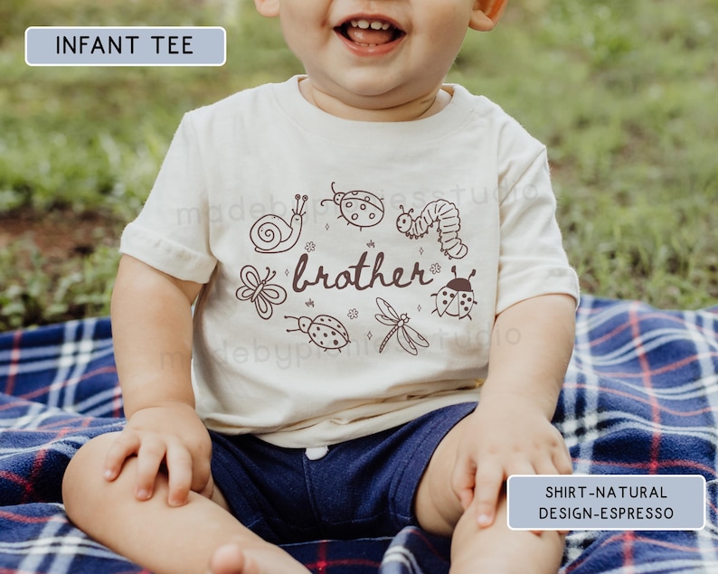 Op de afbeelding: Een cr&egrave;mekleurig baby-T-shirt met een bruine afbeelding van insecten en het woord "brother". Het ontwerp bevat een slak, lieveheersbeestjes, een rups, een vlinder, een libelle en andere insecten. Het kind draagt een marineblauwe korte broek en zit op een blauw geruite deken.
