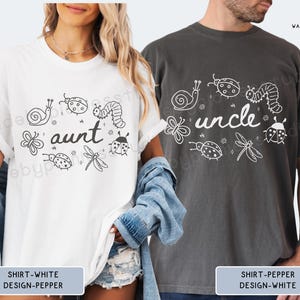 Op de afbeelding: Witte en antracietgrijze t-shirts met de woorden "tante" en "oom" in een speels lettertype, omringd door ge&iuml;llustreerde insecten. Het witte shirt heeft een zwart ontwerp en het antracietgrijze shirt heeft een wit ontwerp.