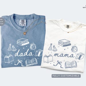 May include: Two t-shirts, one blue and one white, with matching graphic designs. The blue shirt says "dada" and the white shirt says "mama". Both shirts feature book and party hat illustrations, and the year 2026.