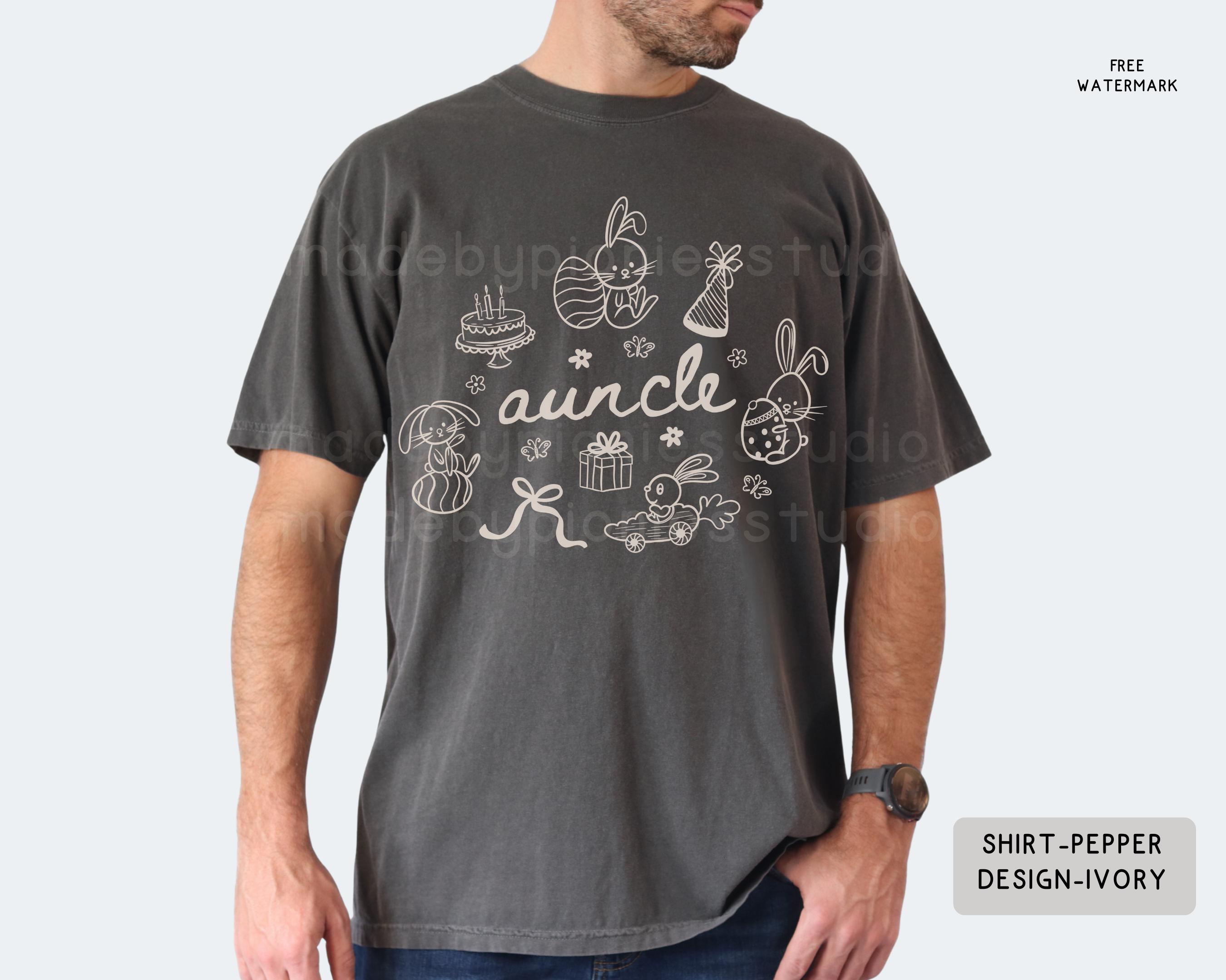 May include: Dark grey t-shirt with a white graphic featuring the word "auncle" and Easter-themed illustrations, including bunnies, eggs, and a cake. The shirt has a relaxed fit and short sleeves.