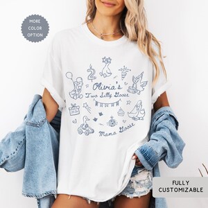May include: White t-shirt with a blue doodle design featuring ducks, balloons, and the text "Olivia's Two Silly Goose". The shirt also has the text "Mama Goose" and "2024". The shirt is fully customizable.
