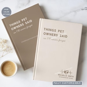 May include: Two hardcover notebooks with the text "THINGS PET OWNERS SAID so I'll never forget". One notebook is taupe, the other is cream-colored. A small coffee cup and sprigs of white flowers are in the image. The cream-colored notebook has a veterinarian's name and logo.