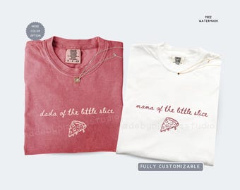 May include: Two folded t-shirts, one red and one white, with text and a pizza slice graphic. The red shirt says "dada of the little slice" and the white shirt says "mama of the little slice". Both shirts have a necklace.