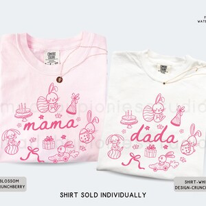May include: Two t-shirts, one pale pink and one white, with matching pink graphic designs. The designs feature Easter bunnies, cakes, gifts, and the words "mama" and "dada". Each shirt has a gold necklace.