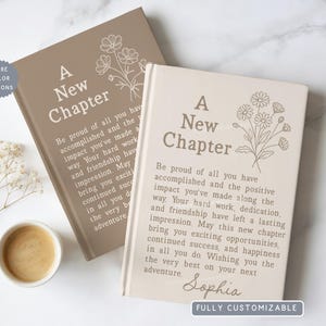 May include: Two hardcover books with beige and taupe covers featuring the text A New Chapter, a line-art floral illustration, and a printed message. The right book includes the name Sophia at the bottom. A small circular badge says More Color Options.