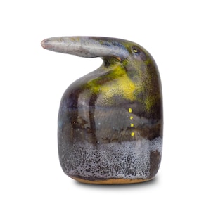 May include: A distinctive ceramic sculpture with a dark, textured finish. It features a curved, beak-like projection and is decorated with yellow and blue highlights. The sculpture has a glossy surface and a small, rounded base.