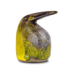 May include: A ceramic sculpture with an abstract design. The piece is a mix of yellow, brown, and grey, creating a textured look. It has a curved, elongated spout. The sculpture is likely handmade, with a unique, artistic appearance.
