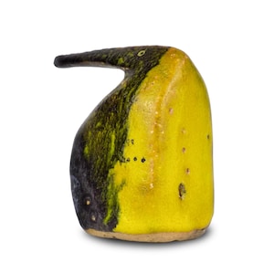 Può includere: Una scultura di uccello in ceramica con un lungo becco curvo. La scultura è principalmente gialla con accenti neri e verdi. Ha una superficie strutturata e un piccolo dettaglio dell'occhio. L'uccello è su una base marrone chiaro.