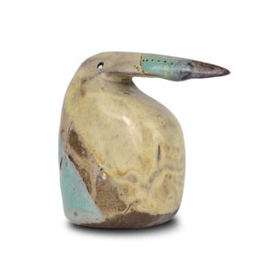 Può includere: Una scultura di uccello in ceramica con un lungo becco. La scultura presenta una tavolozza di colori beige, marrone e turchese. Il becco è di una tonalità di grigio più scura. L'uccello ha un piccolo foro vicino alla sommità.