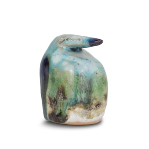 May include: A ceramic bird sculpture with a long beak. The bird is predominantly teal, green, and blue, with dark blue accents and a black beak. The base is light brown. The sculpture is a decorative item.