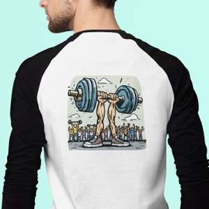 May include: A white and black baseball t-shirt featuring a cartoon illustration of a pair of legs lifting a barbell with a crowd of people cheering in the background.