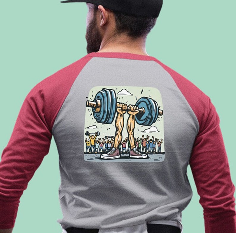 May include: A grey and red baseball t-shirt featuring a cartoon illustration of a pair of legs lifting a barbell with a crowd of people cheering in the background.