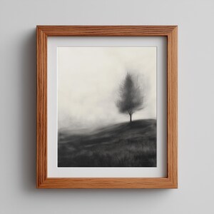 Puede incluir: Una impresión artística en blanco y negro enmarcada que representa un árbol solitario en una colina. La obra de arte tiene un efecto suave y borroso, con un fondo claro y un primer plano oscuro. El marco es de madera.