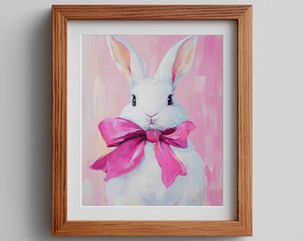 Op de afbeelding: Een ingelijst schilderij van een witte konijn met een grote roze strik. Het konijn staat centraal tegen een roze achtergrond. Het kunstwerk zit in een houten lijst.