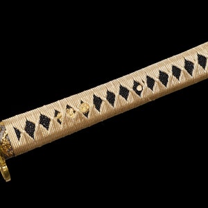 Pode incluir: Close-up de uma espada katana com uma pega tran&ccedil;ada bege e preta. A pega &eacute; envolvida num estilo japon&ecirc;s tradicional com um padr&atilde;o de diamante.