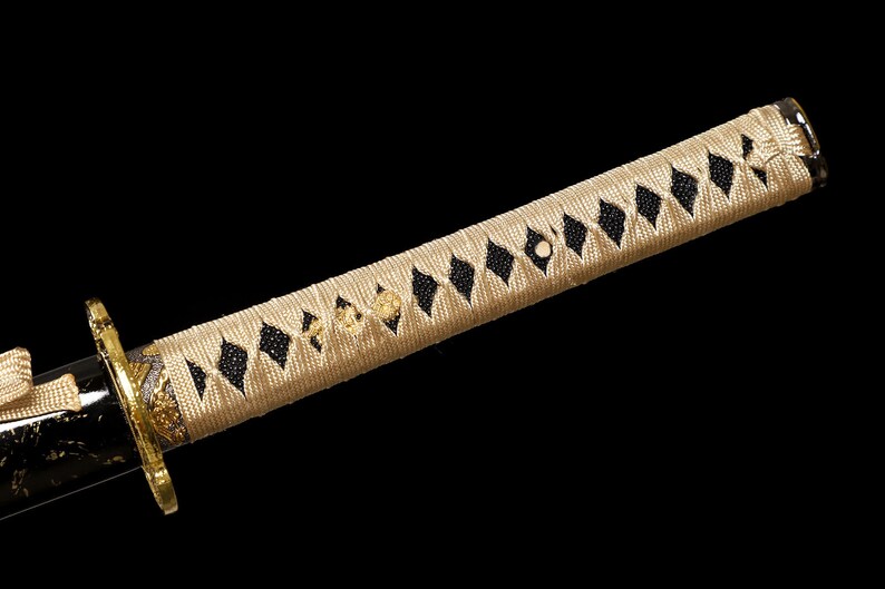 Pode incluir: Close-up de uma espada katana com uma pega tran&ccedil;ada bege e preta. A pega &eacute; envolvida num estilo japon&ecirc;s tradicional com um padr&atilde;o de diamante.