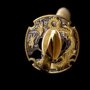 Pode incluir: Um tsuba de espada samurai de ouro e prata, com um design de drag&atilde;o. O tsuba &eacute; de forma circular com uma borda elevada e uma abertura central para a l&acirc;mina.