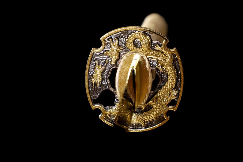 Pode incluir: Um tsuba de espada samurai de ouro e prata, com um design de drag&atilde;o. O tsuba &eacute; de forma circular com uma borda elevada e uma abertura central para a l&acirc;mina.