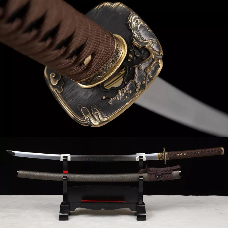May include: An ornate katana sword with a black blade and a decorative handle. The handle is wrapped in brown fabric and features gold-colored accents. The sword is displayed on a black stand, with its scabbard visible below.