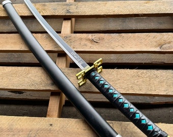 May include: A black katana sword with a gold and turquoise patterned handle. The sword is on a wooden surface.