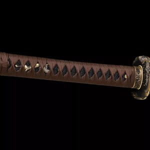 May include: Close-up of a katana handle, featuring a brown, tightly wrapped grip with diamond-shaped black accents. The handle's end has a gold-colored cap, and the guard is a dark metal with gold detailing. The background is solid black.