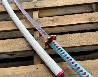 May include: A white and pink katana with a blue and pink patterned handle. The blade has a pink and black design and the handle has a pink flower design. The katana is resting on a wooden surface.