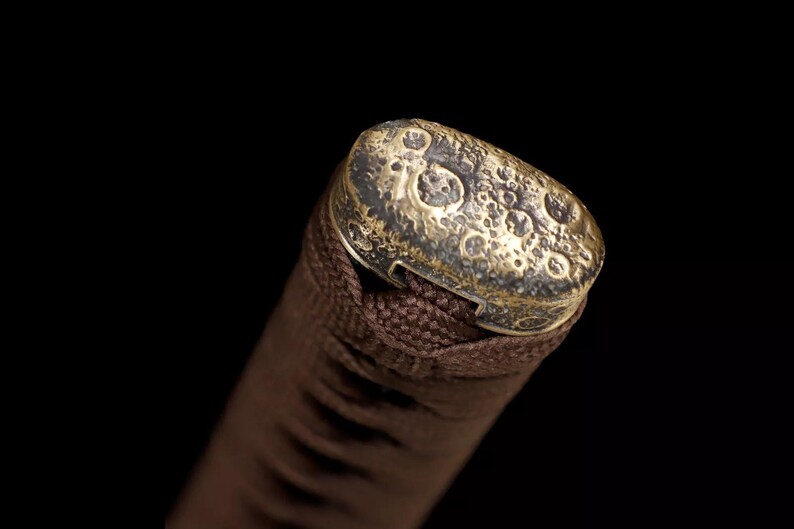 May include: Close-up of a brown handle with a textured, gold-colored cap. The cap has a pattern of small, irregular circles. The handle appears to be wrapped in a woven, brown material, suggesting a decorative or functional item.