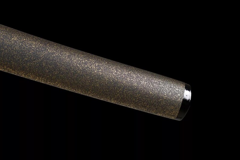 May include: Close-up of a metallic, cylindrical object with a speckled, textured surface in shades of gold and black. The object has a black band and a silver end cap. The background is solid black.