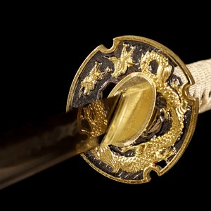Pode incluir: Close-up de uma espada katana com um design de drag&atilde;o dourado e preto na tsuba, ou guarda.