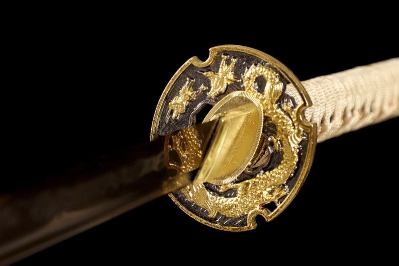 Pode incluir: Close-up de uma espada katana com um design de drag&atilde;o dourado e preto na tsuba, ou guarda.