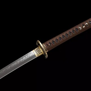 May include: A Japanese katana sword with a brown handle and a silver blade. The handle is wrapped in a dark brown material and features a decorative gold-colored guard. The blade has an etched design.