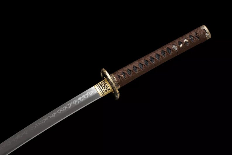 May include: A Japanese katana sword with a brown handle and a silver blade. The handle is wrapped in a dark brown material and features a decorative gold-colored guard. The blade has an etched design.