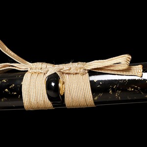 Pode incluir: Um close-up de uma bainha de katana preta e dourada com um cord&atilde;o bege enrolado ao redor.